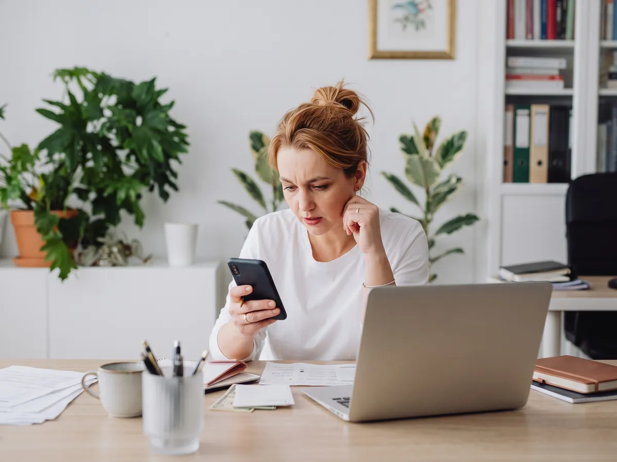 Owner at work checking her phone with a worried look, thinking about her anxious dog at home in Rhode Island